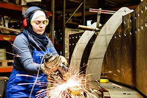 Young female trainee works with a grinder in a workshop, flying sparks 